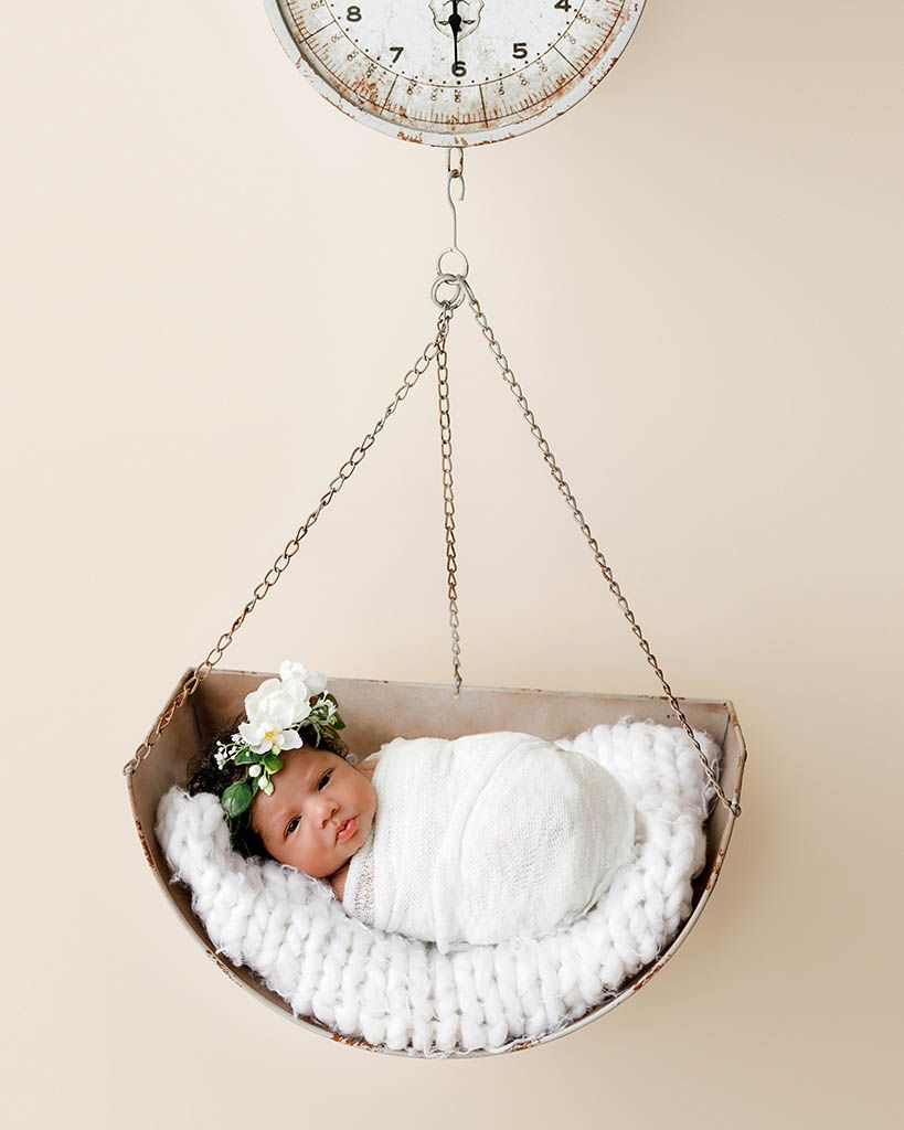 Newborn baby swaddled in white lying in vintage scale basket by Perris newborn photographer.