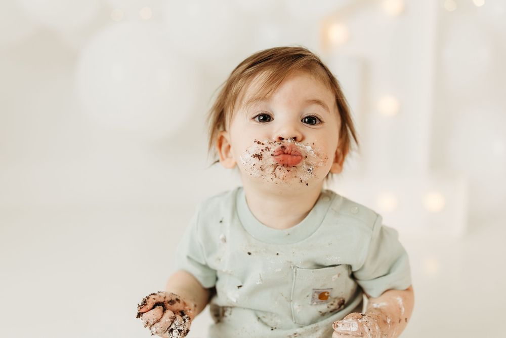 Messy baby with chocolate cake on face and hands during first birthday cake smash photo session.