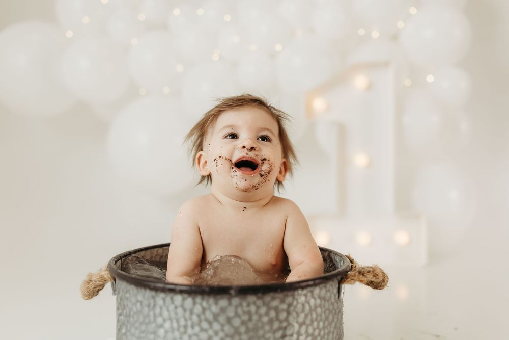 Happy baby laughing in vintage metal tub during first birthday cake smash photoshoot.