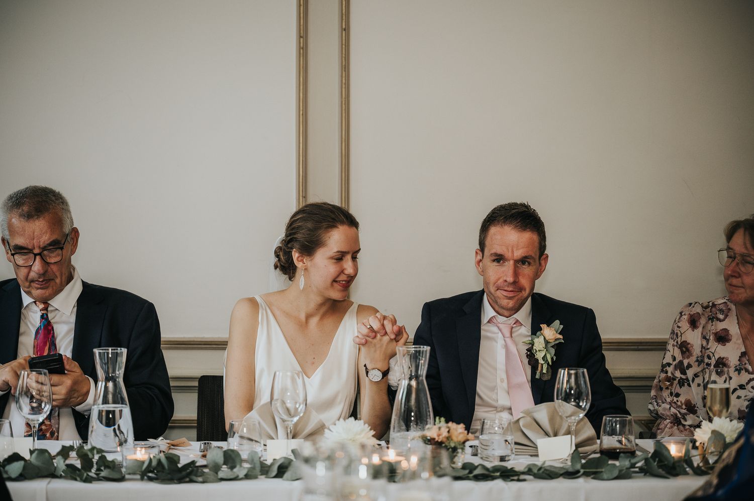 Couple sharing romantic moment on boat deck at sunset, bride in lace gown, groom in gray suit, floral arrangements nearby.
