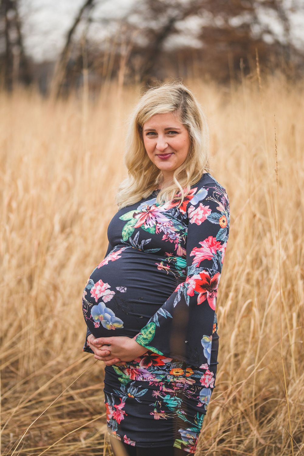 Pregnant woman in floral dress holding baby bump in golden field.