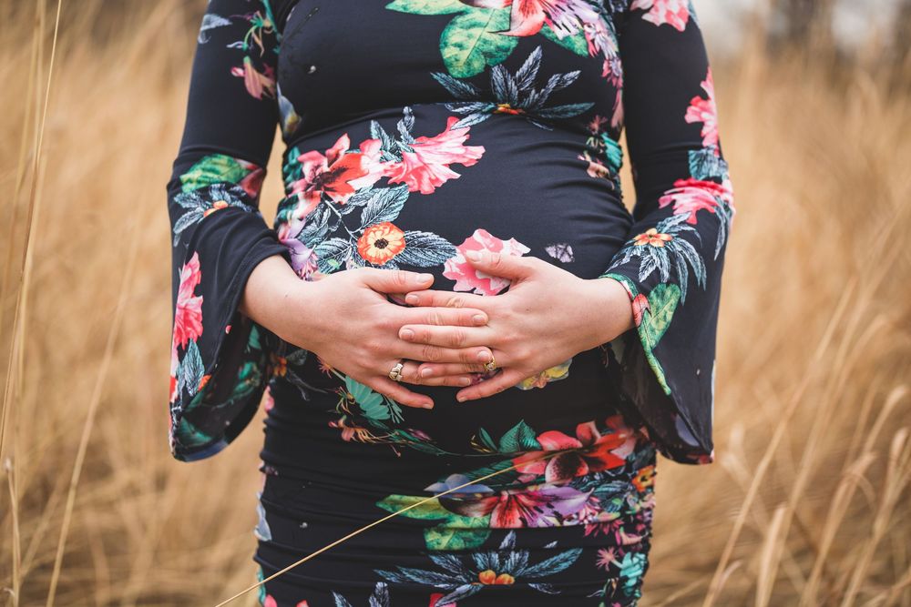 Pregnant woman in floral dress cradling baby bump in golden field.