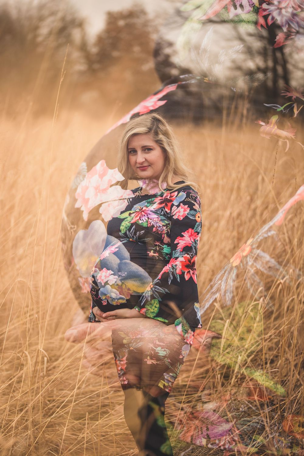 Pregnant woman in floral dress poses in golden field with dreamy double exposure effect.