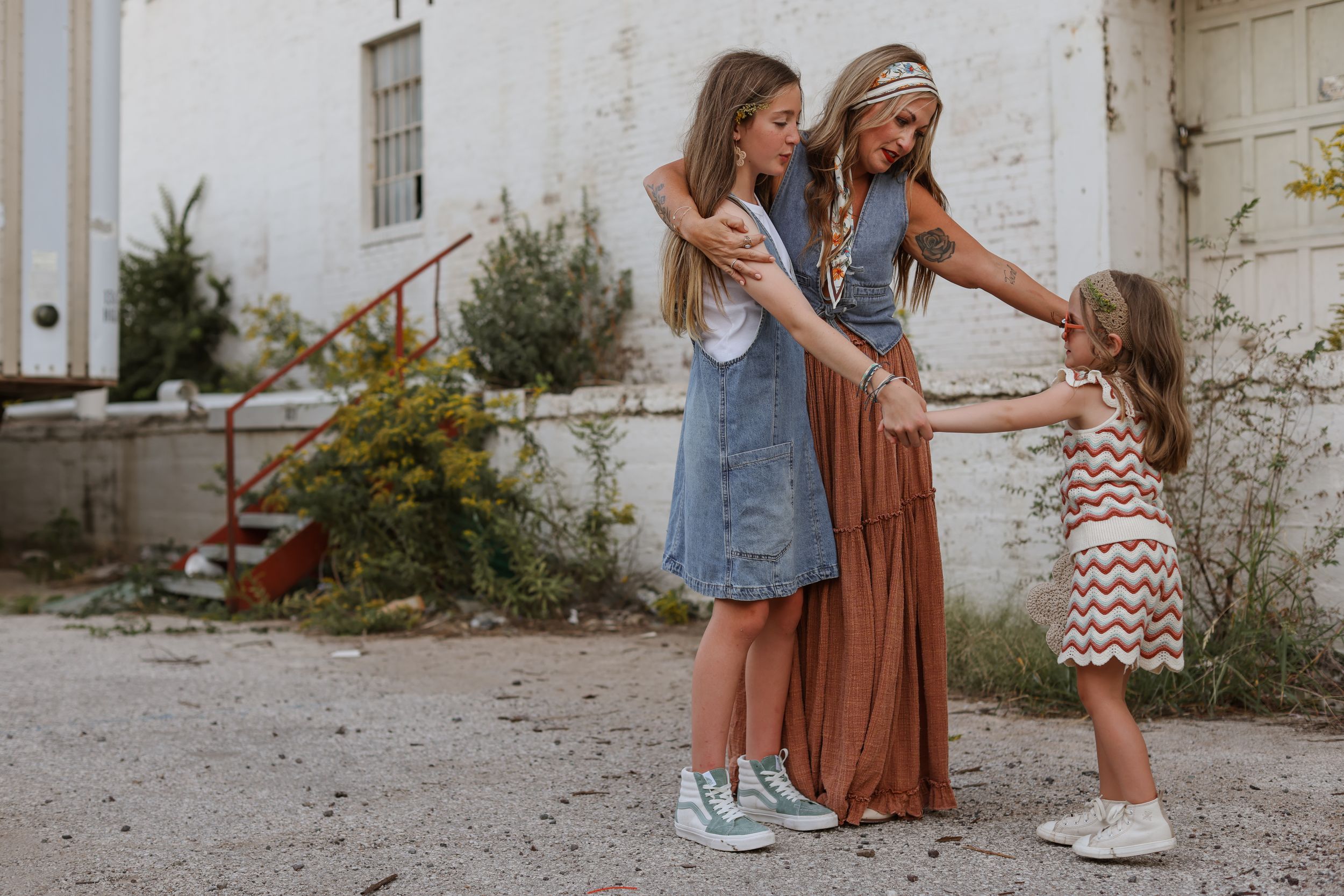 A mother holds hands with her young teenage and elementary-aged daughters and looks at them lovingly during a West Bottoms family photoshoot