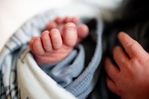 Macro close-up of delicate newborn baby toes wrapped in a soft blue personalized name swaddle blanket.