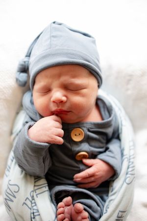 Newborn baby Samuel sleeping in blue button outfit and knotted hat with personalized name swaddle blanket.