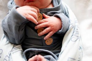 Close-up of newborn baby hands grasping blue outfit with wooden buttons.