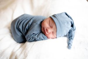 Peaceful newborn baby sleeping in blue pajamas and knotted hat on white bedding.