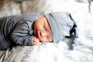 Sleeping newborn baby in gray pajamas and hat resting on personalized name blanket.