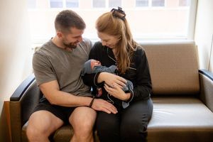 New parents sitting together on hospital couch lovingly holding their newborn baby.