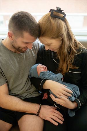 Happy new parents leaning in close together admiring their newborn baby in hospital room.