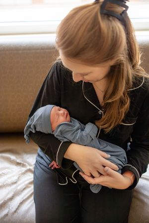 New mother in black pajamas gently cradling sleeping newborn baby dressed in blue.