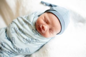 Close-up of sleeping newborn Samuel wrapped in a light blue personalized name swaddle blanket and hat.