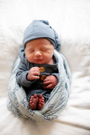 Peaceful newborn baby in blue outfit and hat swaddled in personalized Samuel blanket with tiny toes visible.