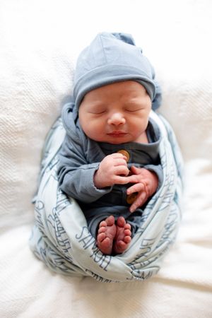 Sleeping newborn baby Samuel in blue outfit and knotted hat wrapped in personalized name swaddle blanket.