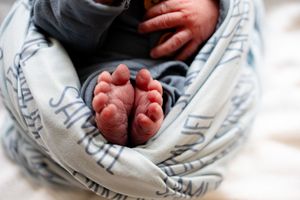 Close-up of tiny newborn baby feet peeking out of a personalized blue Samuel name swaddle blanket.