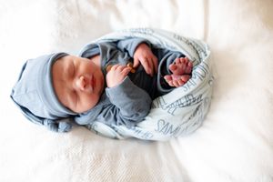 Sleeping newborn baby in blue outfit and hat loosely wrapped in a personalized Samuel name blanket.
