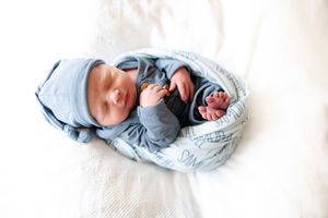 Newborn baby Samuel sleeping peacefully in blue knotted hat and personalized name swaddle blanket.