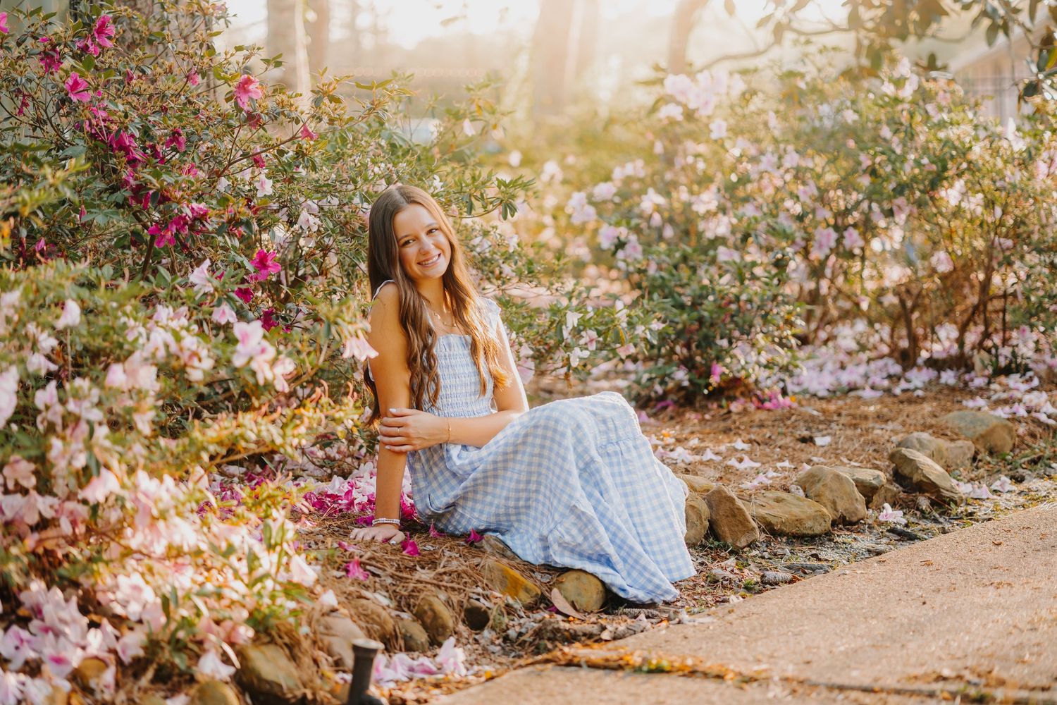 Young woman in maroon sweater leans on rustic wooden fence during golden hour outdoor photo session.