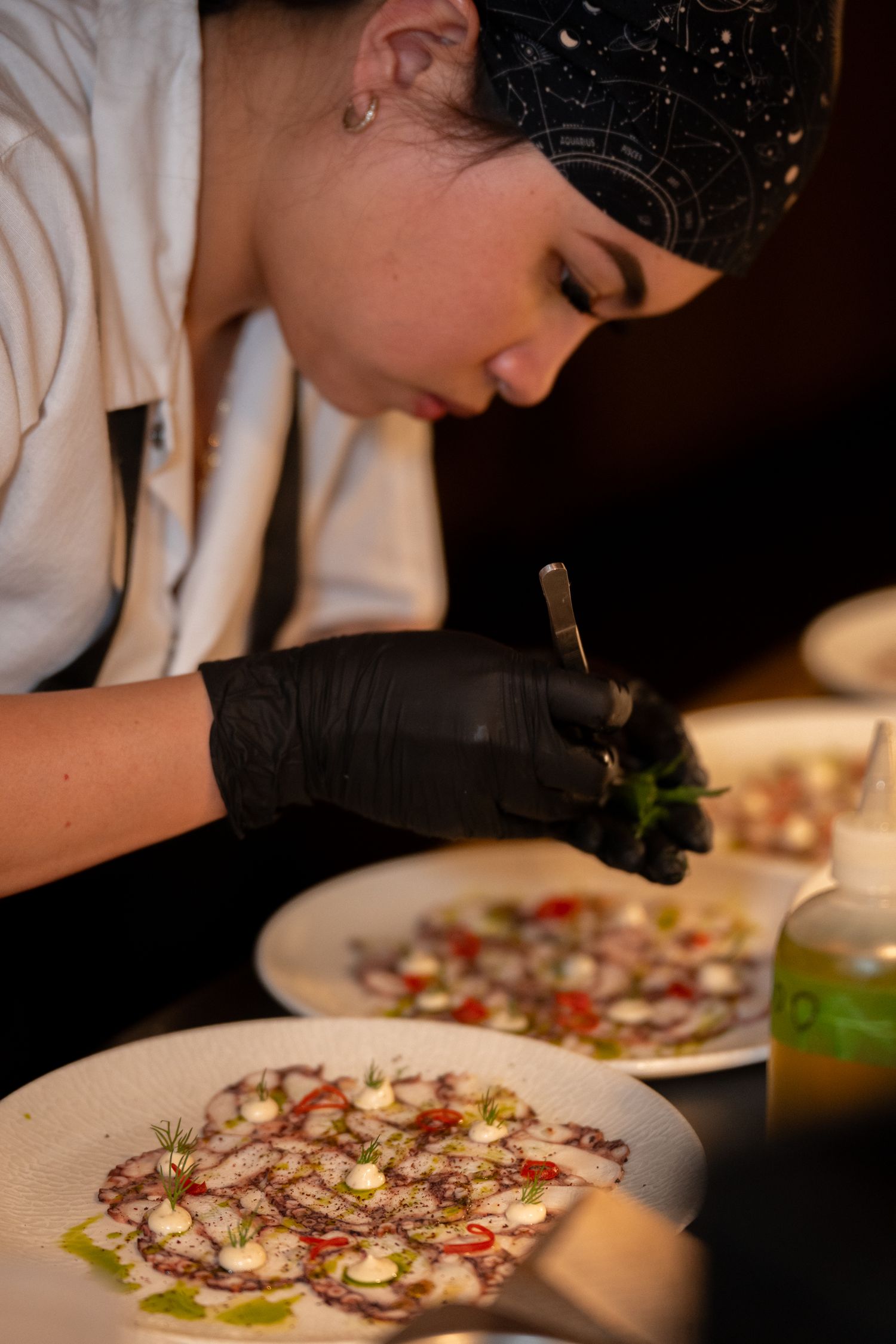 Chef carefully plating a beautifully garnished dish with delicate precision in a professional restaurant kitchen.