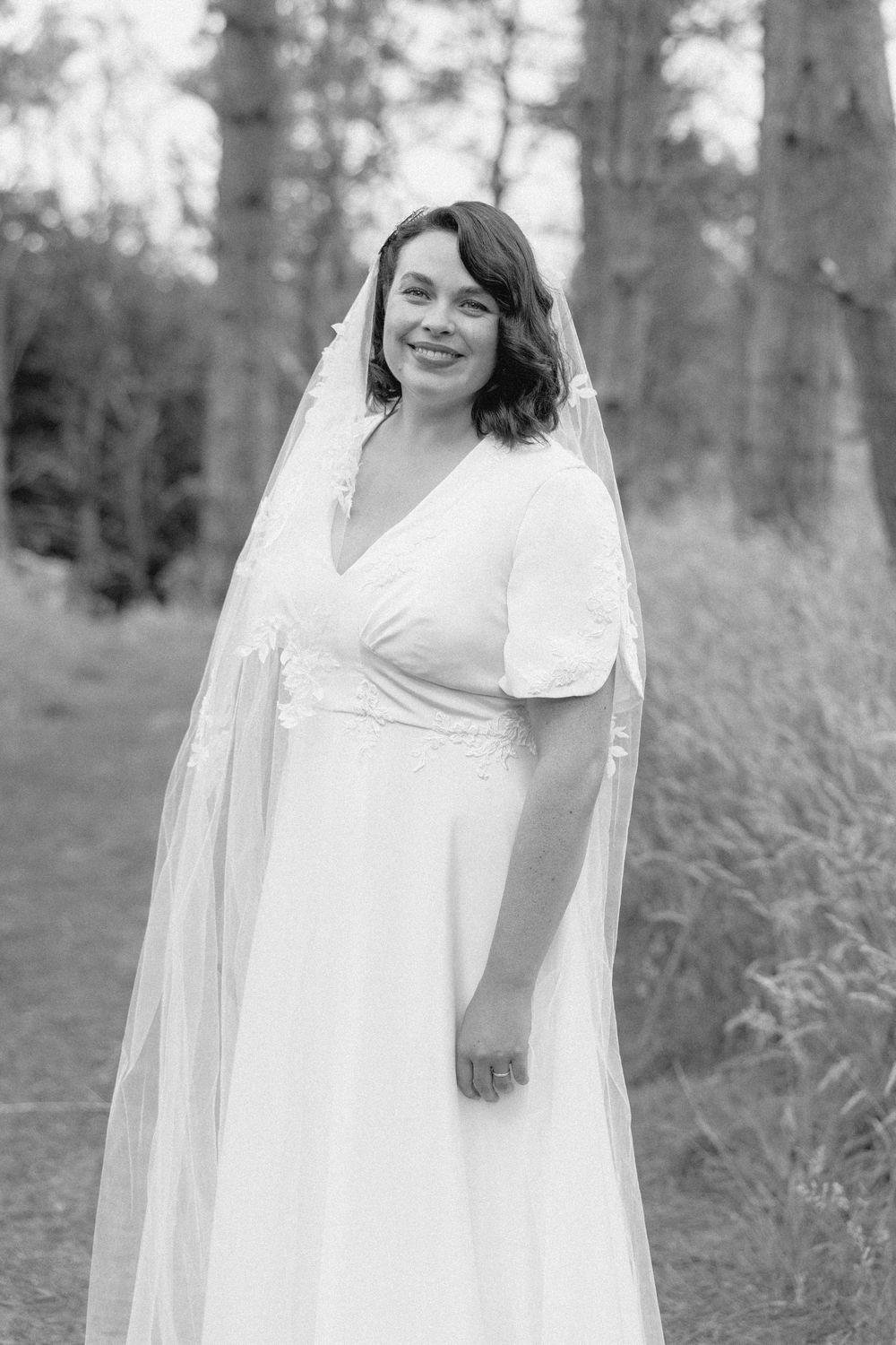Black and white outdoor bridal portraits showing a smiling bride in a flowing white dress and veil in a wooded setting.