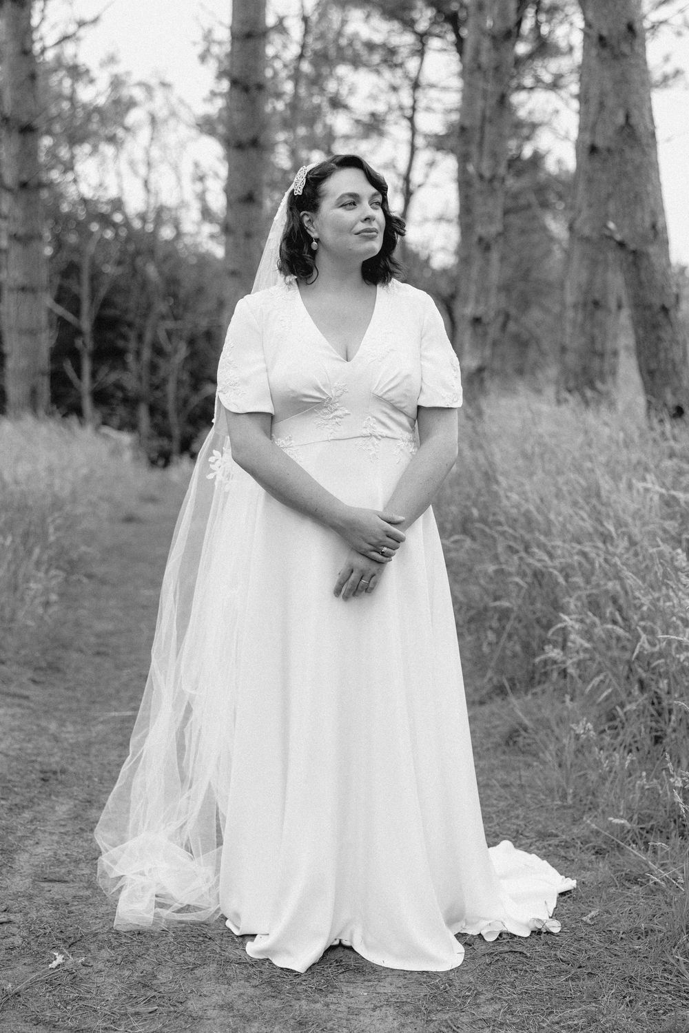 Black and white photo series showing a person in a flowing white dress sitting gracefully on grass near trees.