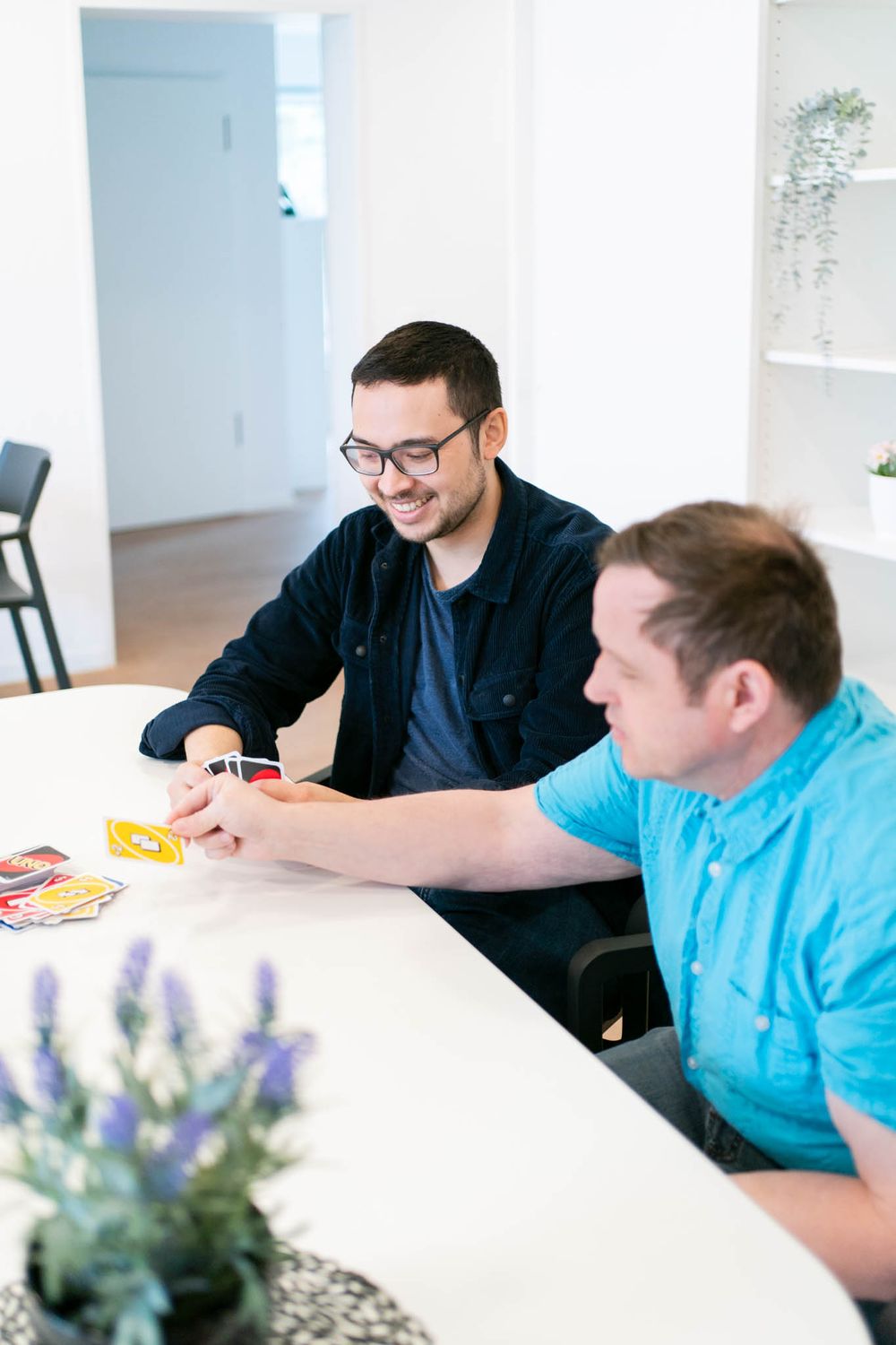 Two people sitting at a white table having a conversation with a lavender plant decoration in the foreground.