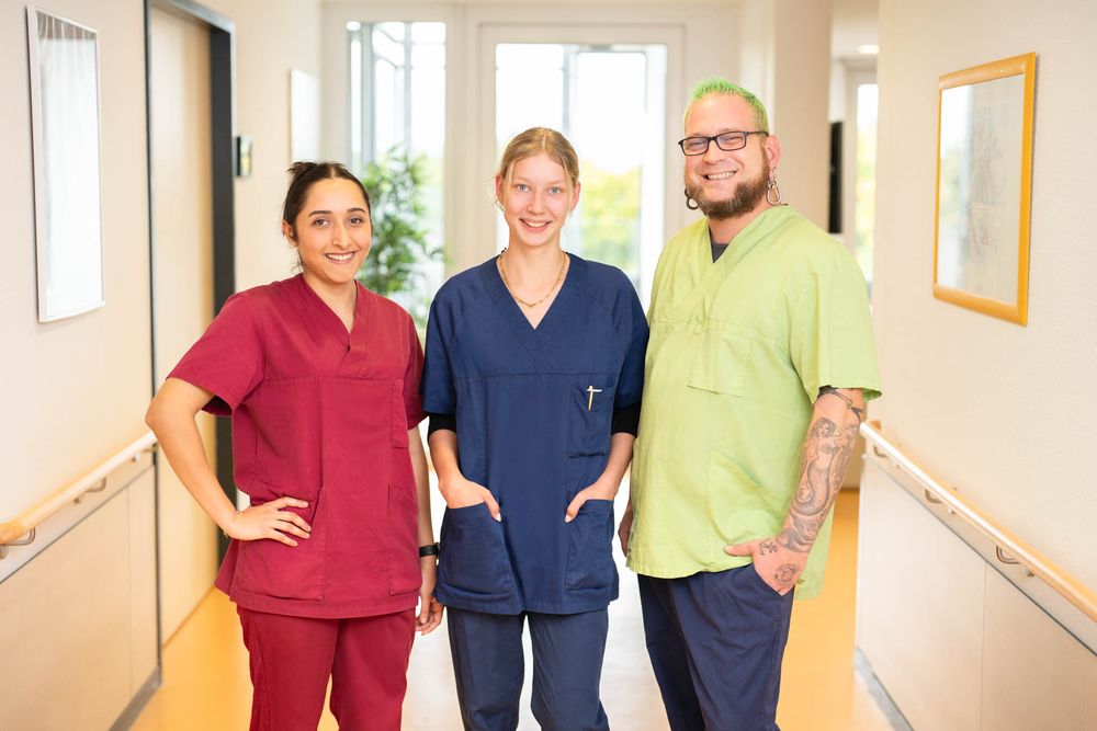 Medical staff in colorful scrubs stand together smiling in a bright hospital hallway.