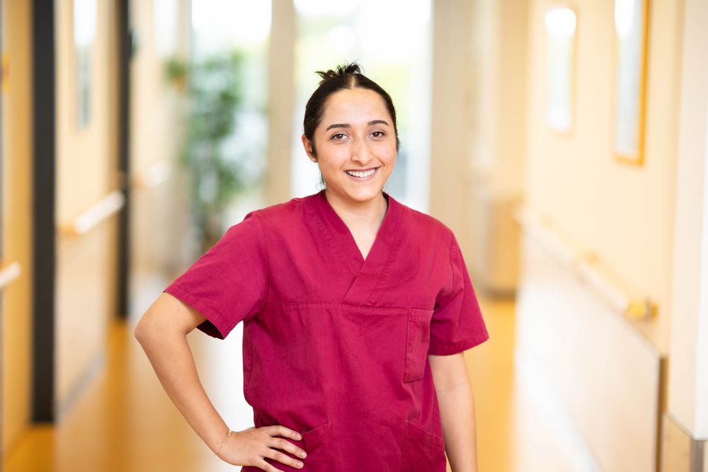 Healthcare professional in burgundy scrubs standing confidently in a bright medical facility hallway.