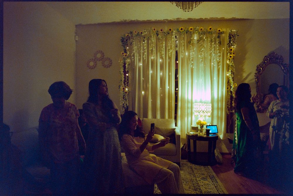 Women gathered in a warmly lit room decorated with fairy lights and curtains during a festive celebration.