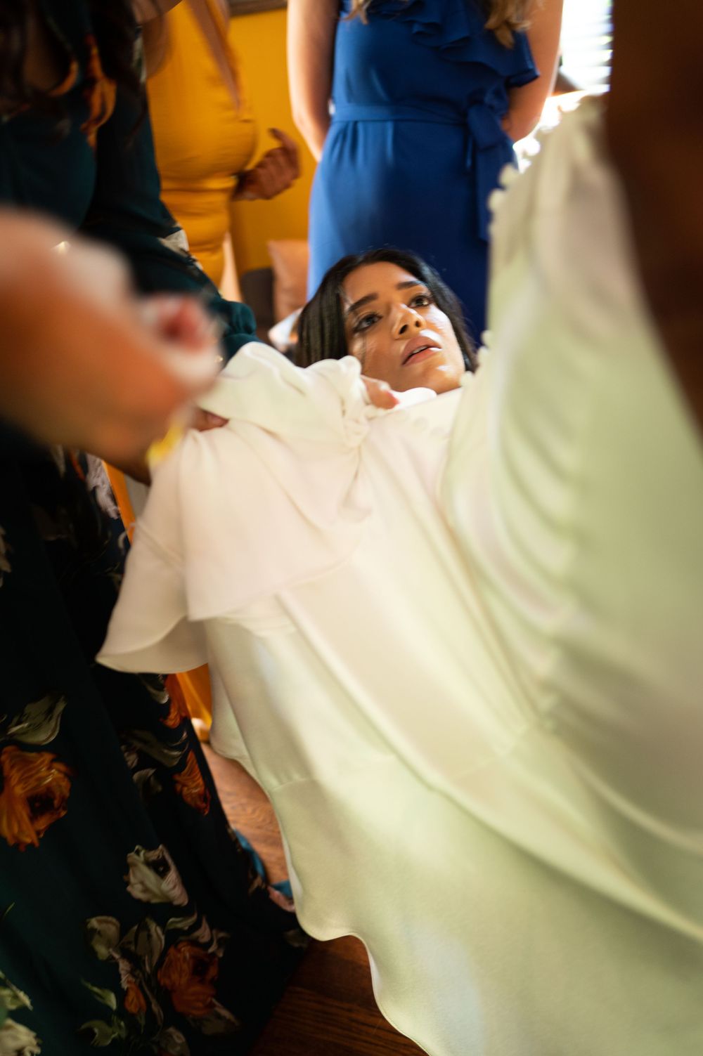Close-up shot of bride in white dress looking up while attendants adjust her gown before wedding.