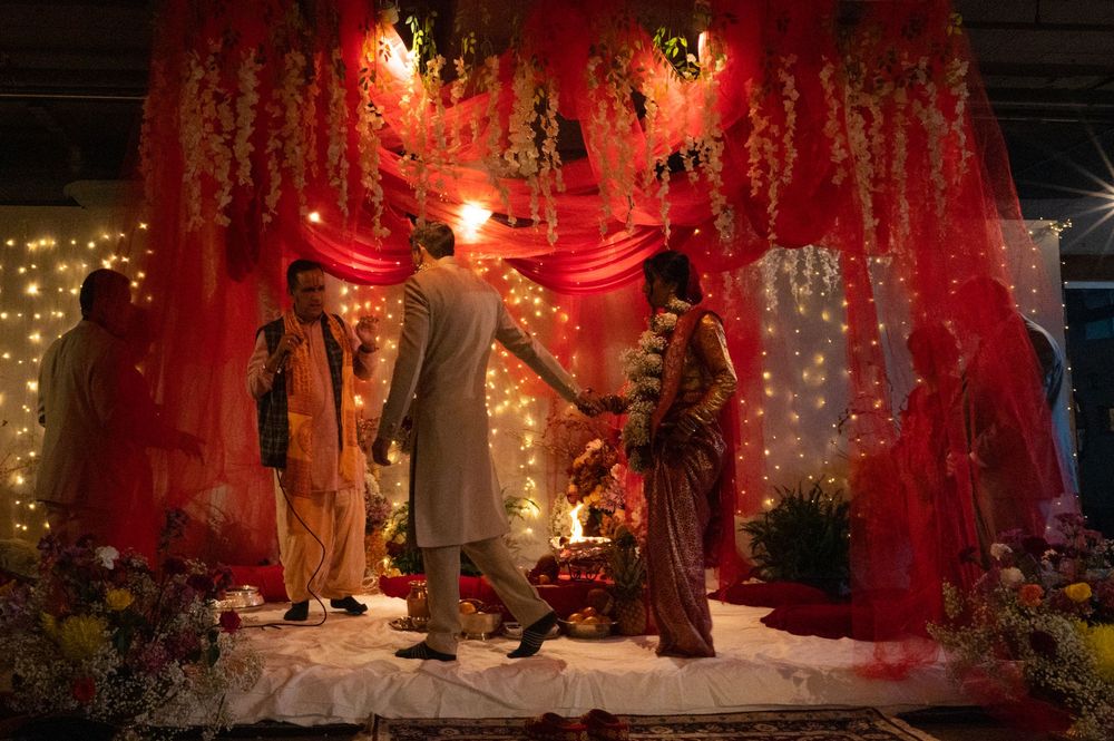 A bride and groom perform traditional rituals on a decorated stage at a Hindu wedding ceremony.