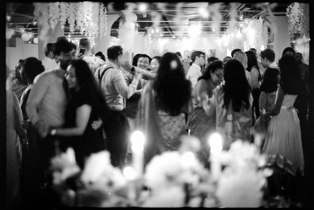 Black and white photo of guests dancing and celebrating at a crowded elegant wedding reception.