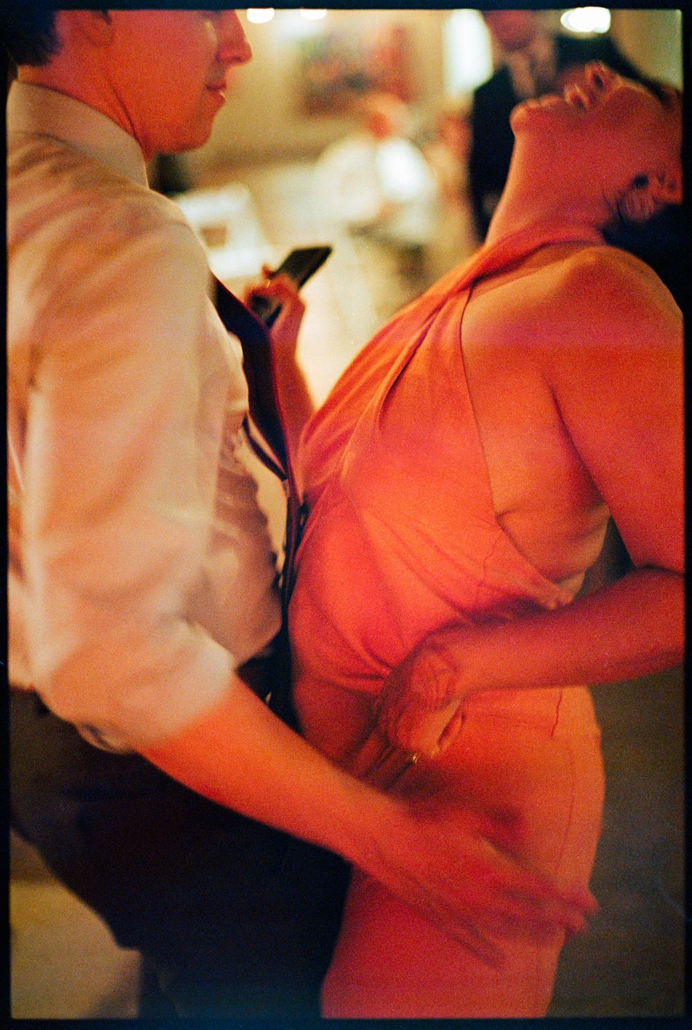 Couple dancing closely at a wedding reception, woman in red dress leaning back.