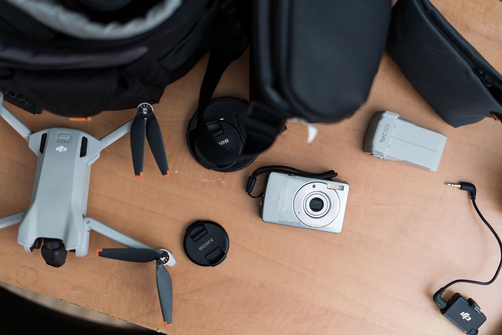 Flat lay of a DJI Mini drone, compact camera, lenses, batteries, and accessories on a wooden surface.