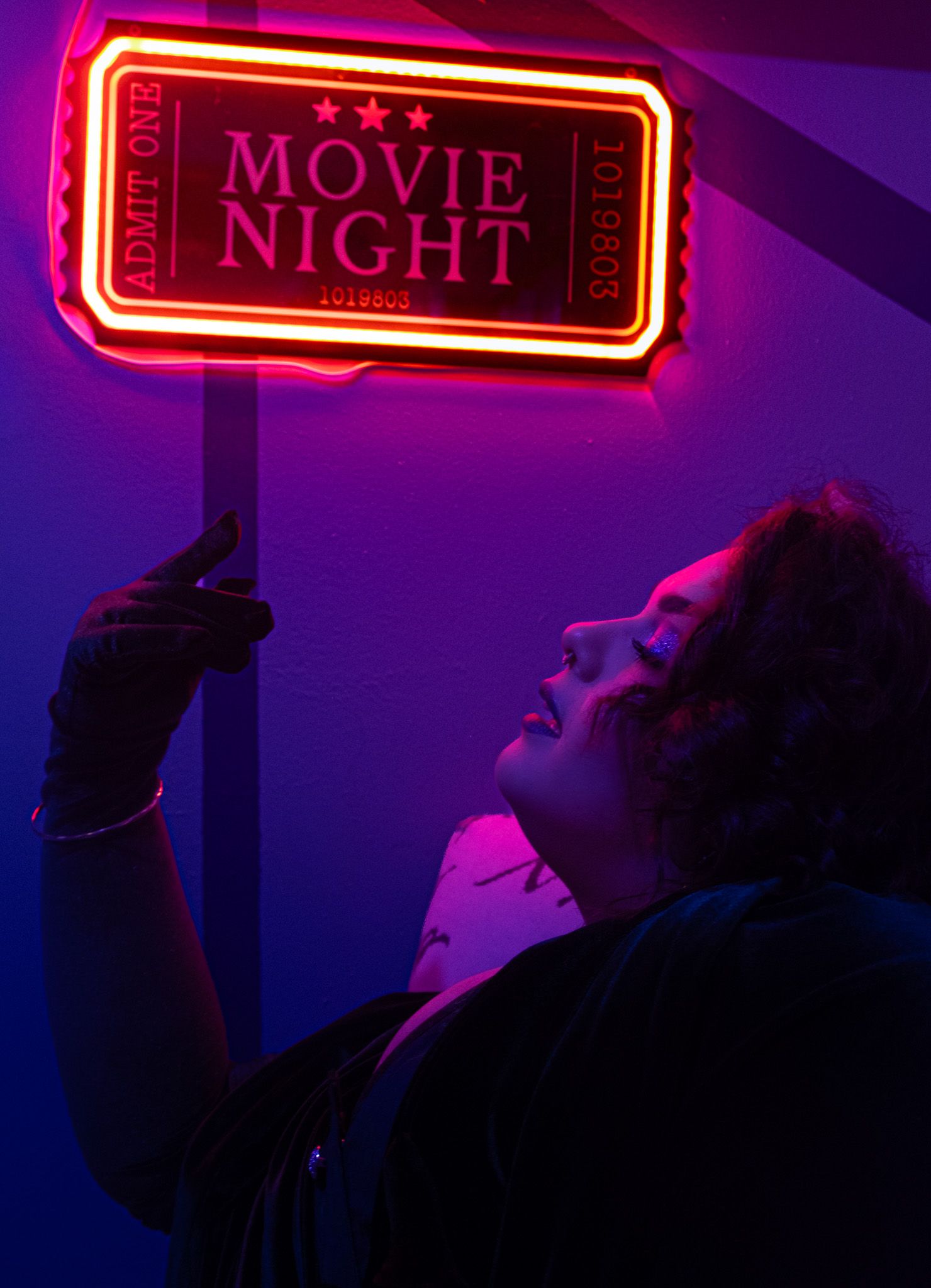 A silhouetted figure illuminated by a neon red 'MOVIE NIGHT' sign against a dark purple background.