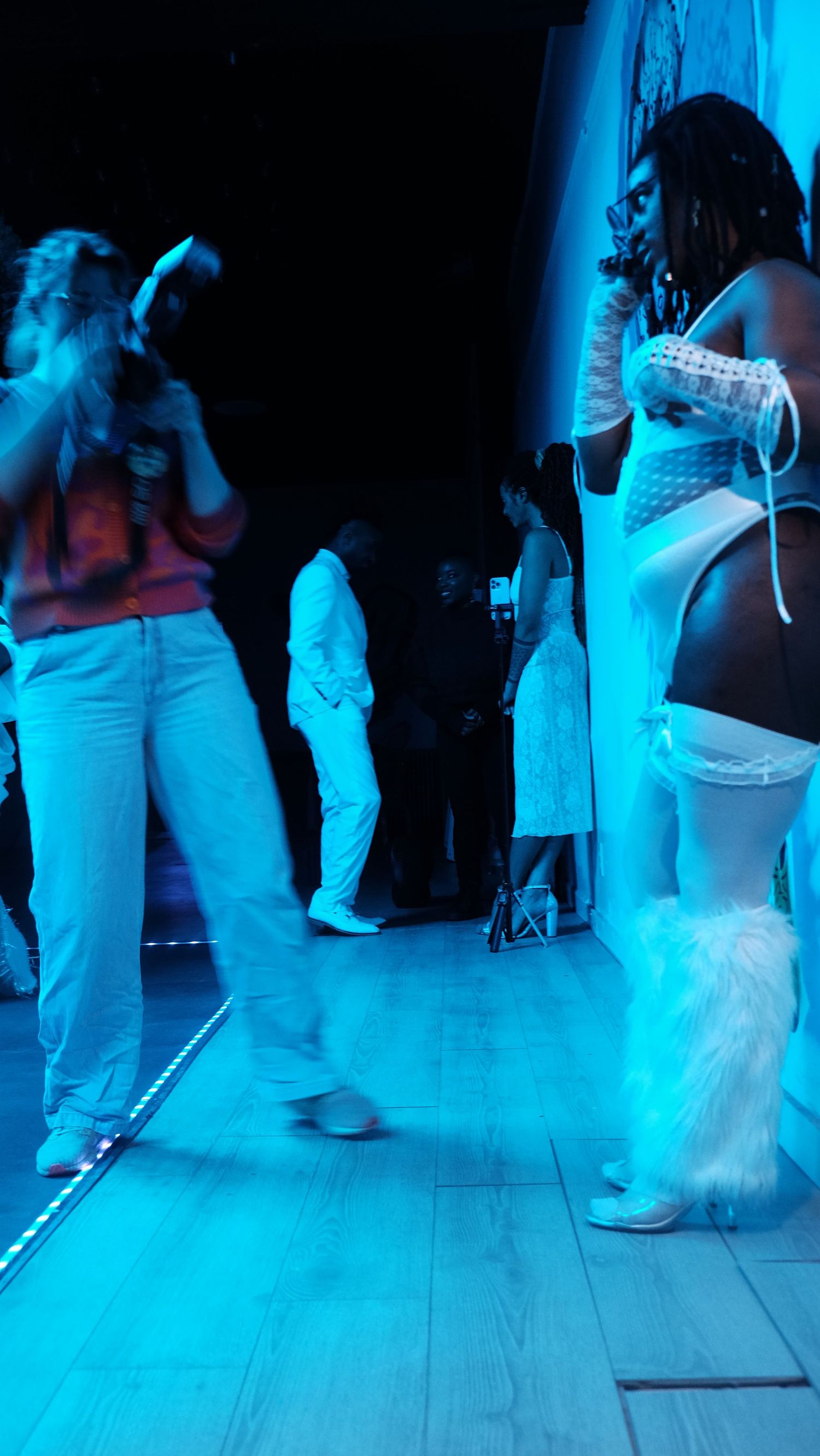 People dancing at a nightclub bathed in blue lighting on a wooden dance floor during an evening event.