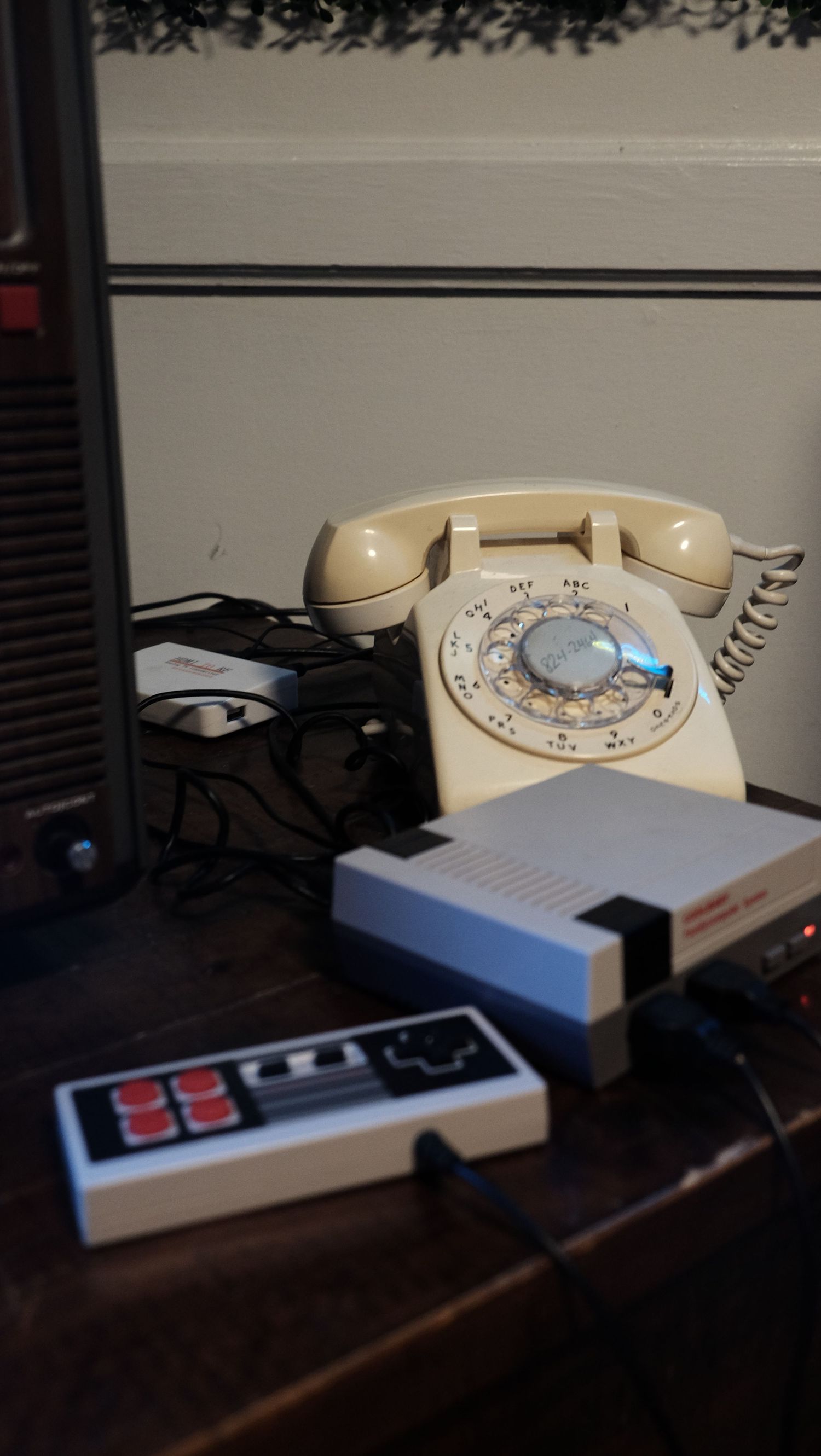 A vintage rotary telephone sits next to a retro Nintendo game controller on a dark wooden surface.