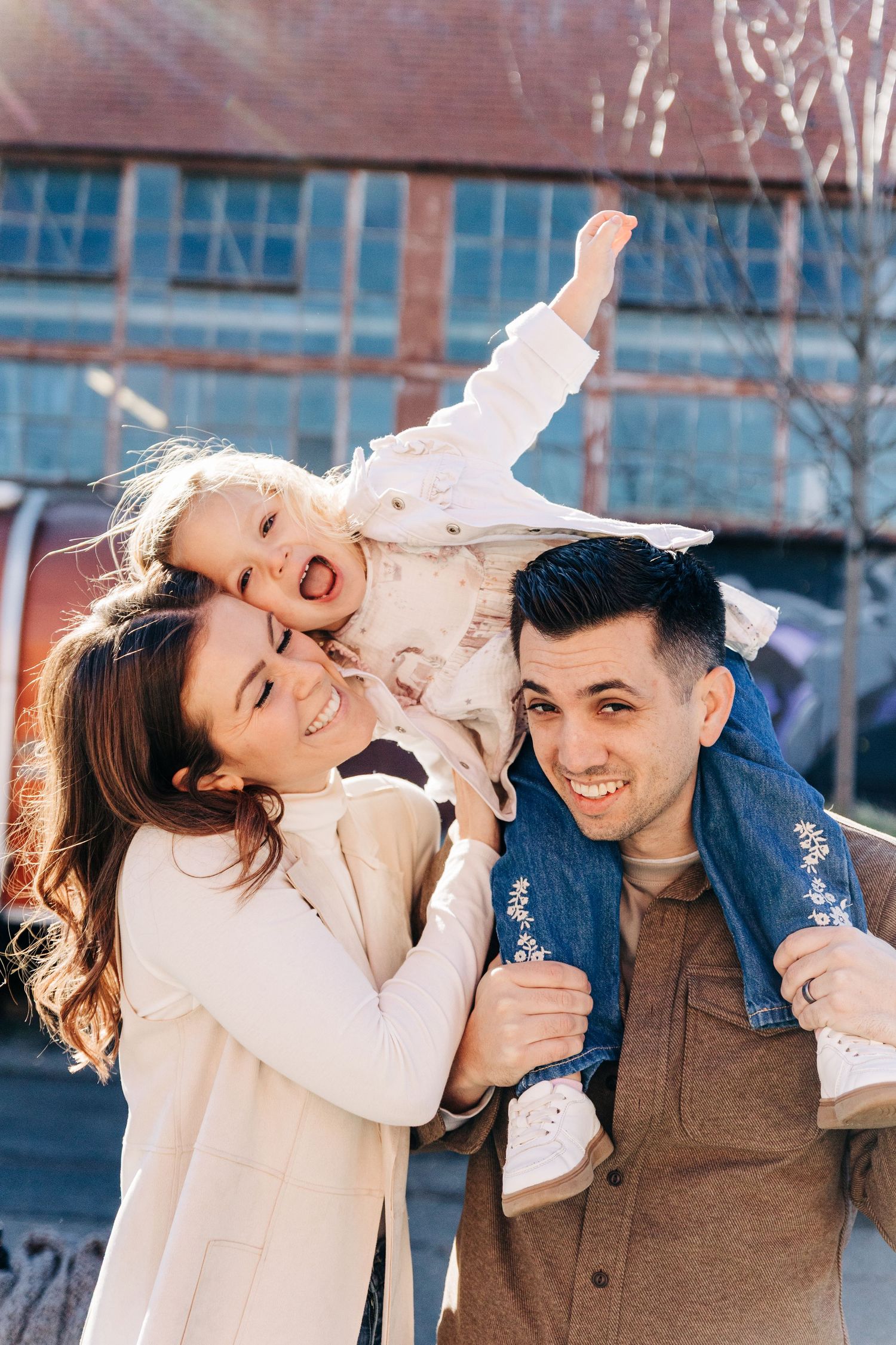 A playful couple laughs and embraces their toddler while enjoying a winter day outdoors.