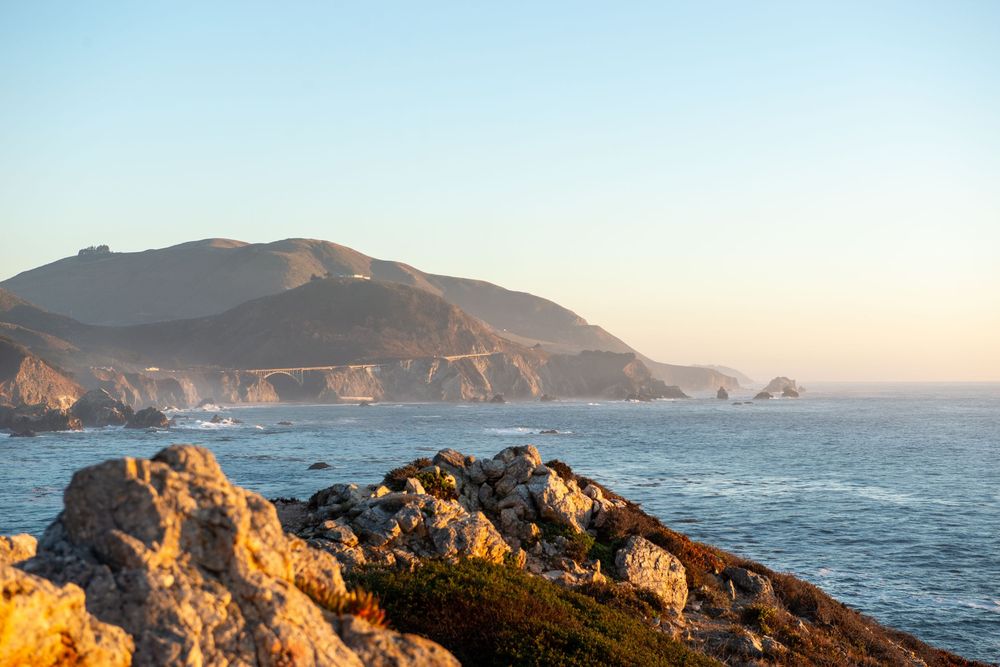 Panoramic view of rugged coastal cliffs and mountains along the Pacific Ocean at sunset.