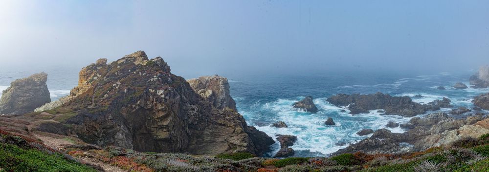 Dramatic coastal landscape featuring rugged cliffs and crashing waves against rocky shores under cloudy skies.