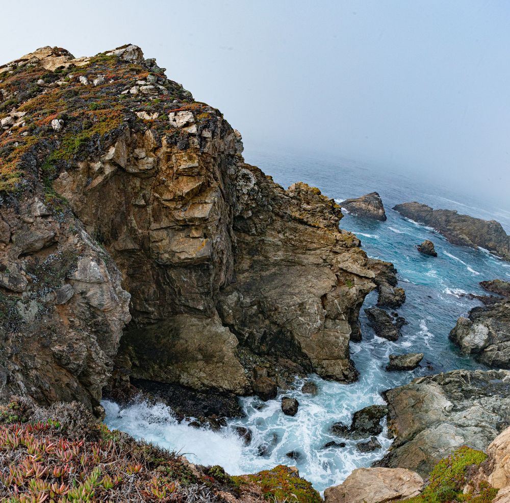 Dramatic coastal cliffs and rock formations along the Pacific Ocean with crashing waves and rugged coastline.