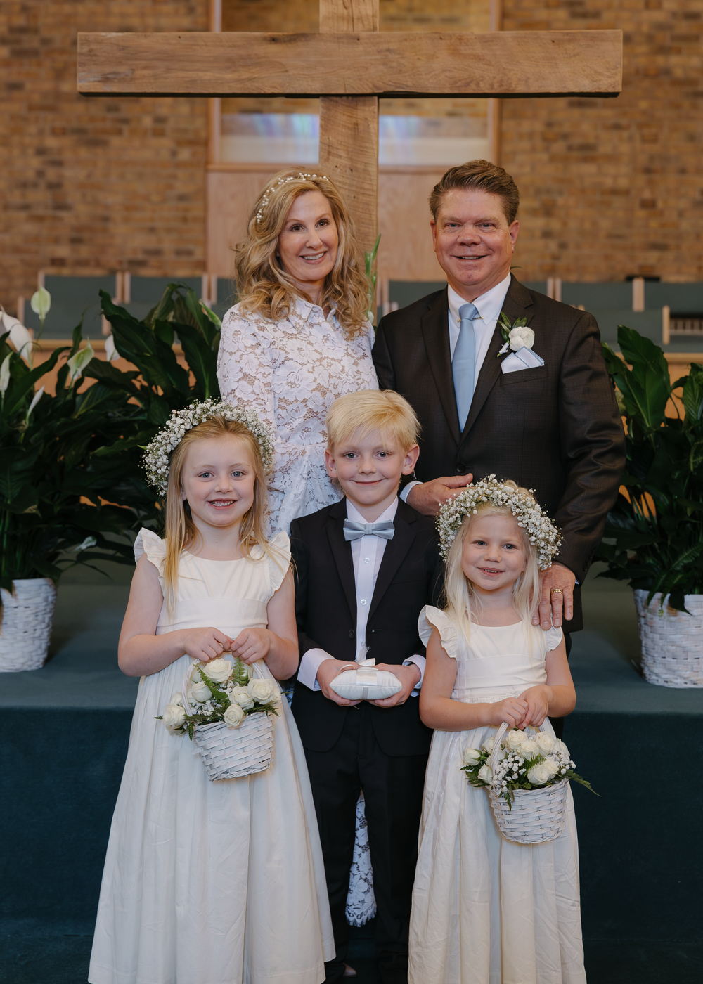 Wedding couple poses with three young flower girls and ring bearer in front of church altar.