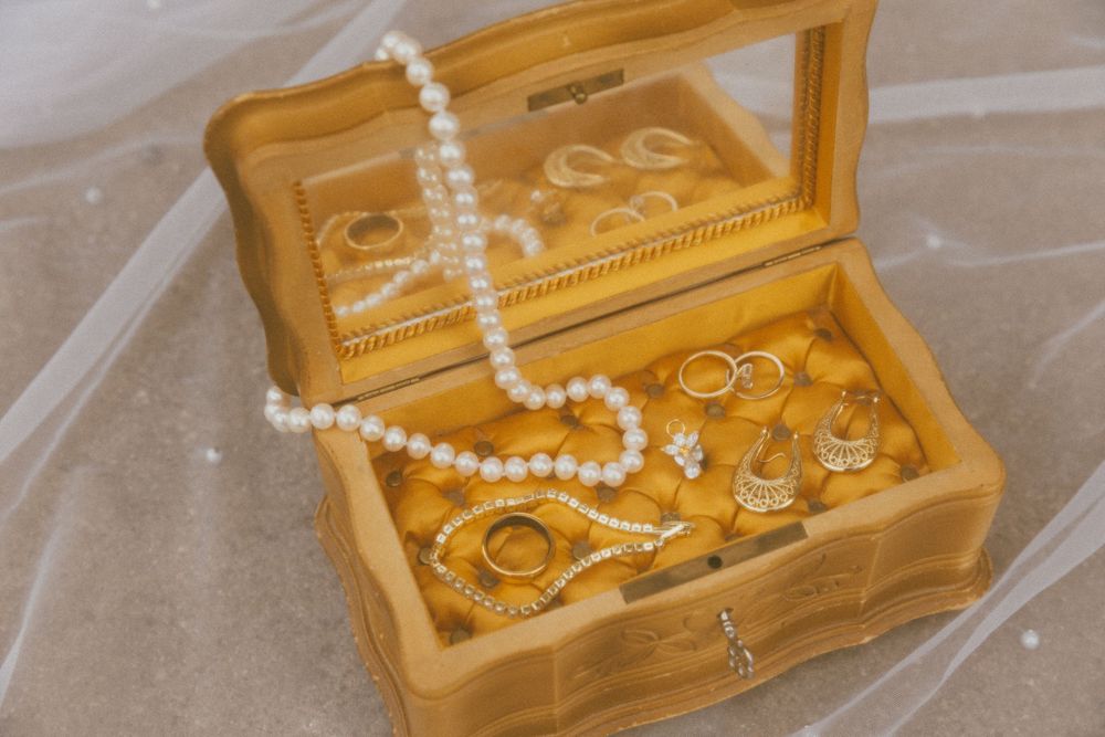 Wooden jewelry box with pearl necklaces and wedding rings displayed.