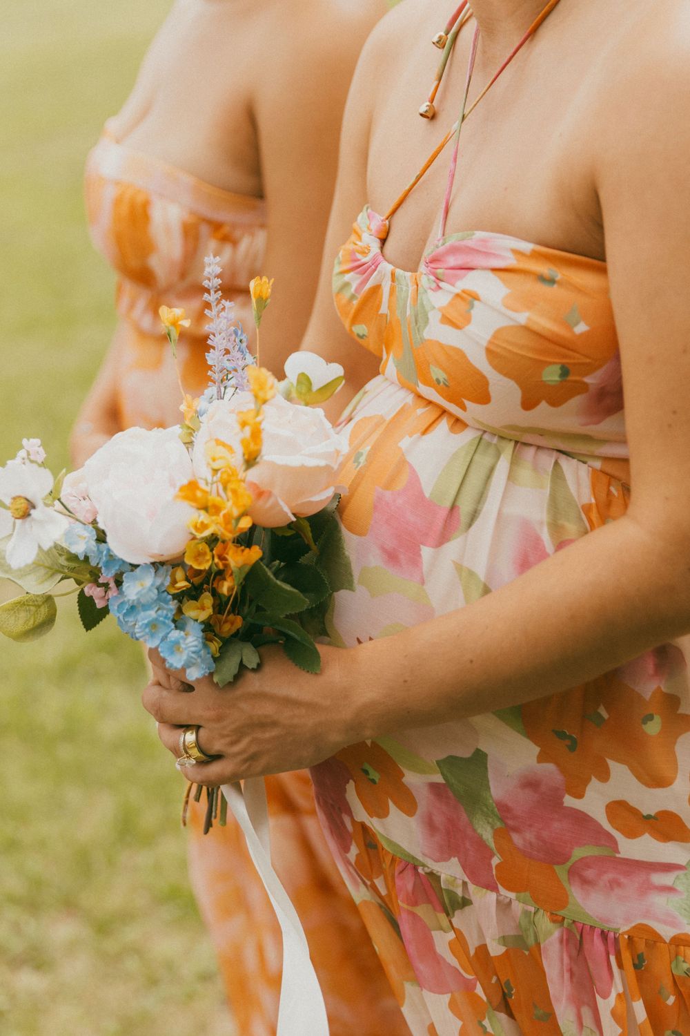 Bridesmaids holding colorful floral bouquets in orange floral print dresses.
