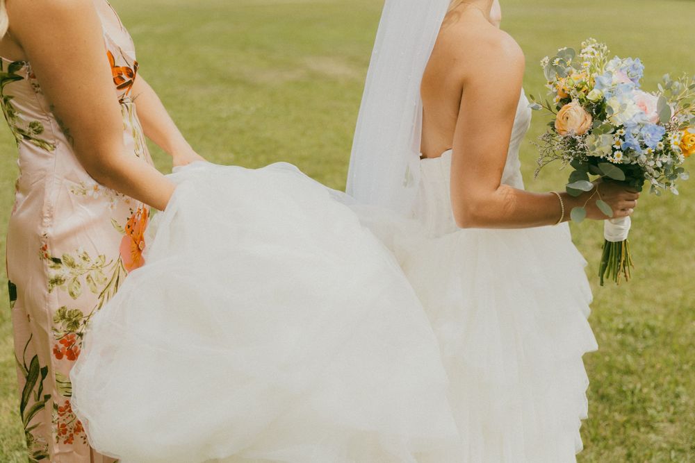 A romantic wedding couple poses in a grassy field with bridesmaids wearing floral dresses.