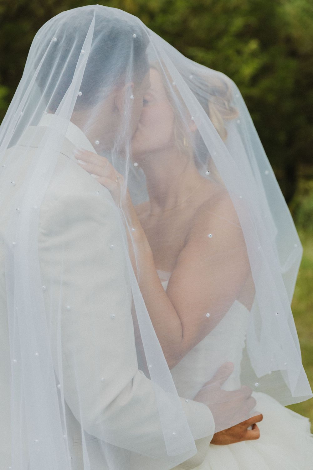 A romantic moment under a delicate white wedding veil in a garden setting.