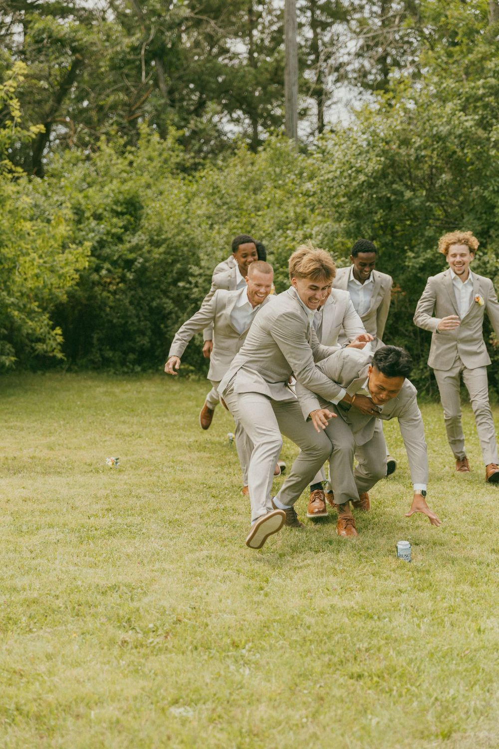 Wedding party members in gray suits race across grass in a fun action shot.