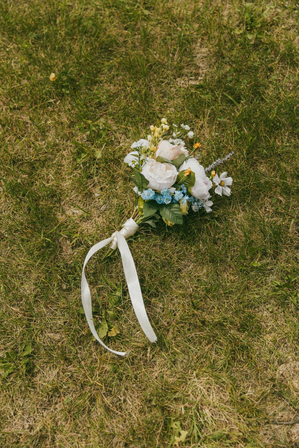White floral boutonnieres with blue accents lying on grass.