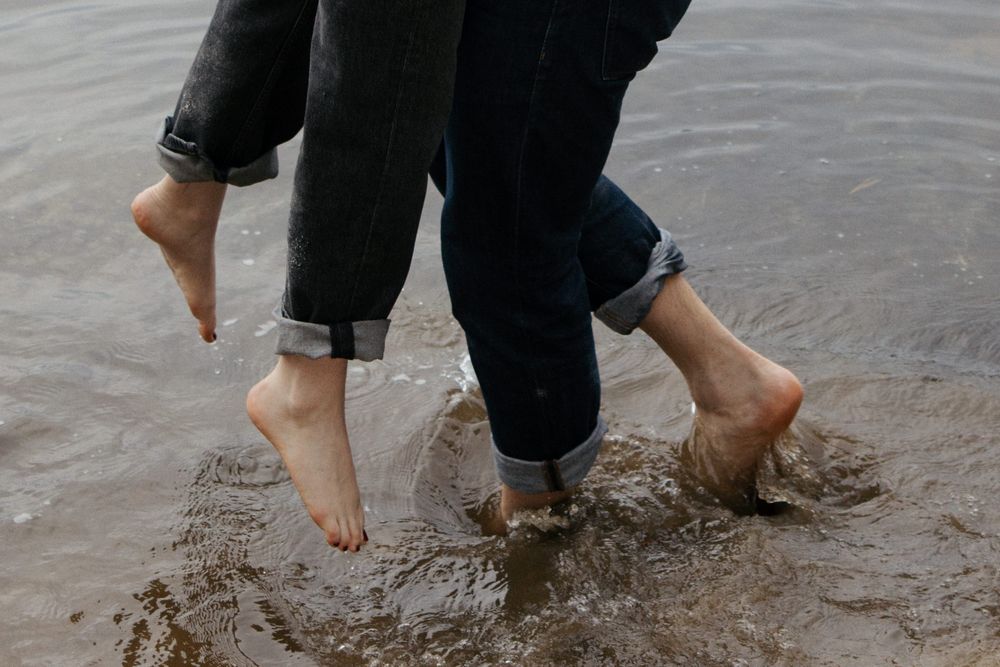 Close-up of couple's bare feet with rolled jeans splashing in shallow water.